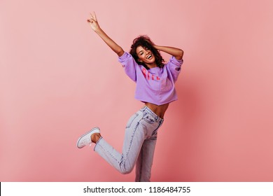 Shapely jocund girl dancing on rosy background. Good-humoured african lady jumping with smile.