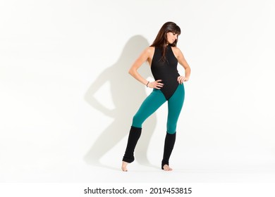Shapely young woman wearing an 80s dance outfit with leotard over tights and leg warmers posing over a white background with shadow and copyspace