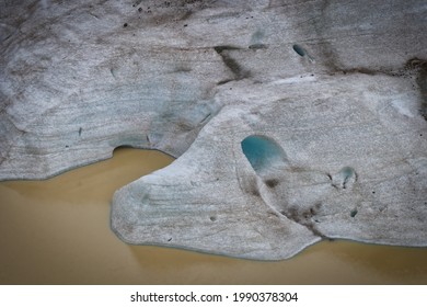 The shapes of the glacier reveal rounded lines zebra with volcanic ash. A cave illuminated by the blue of the ice might suggest that a Troll has taken up residence there. The brown waters of the glaci
