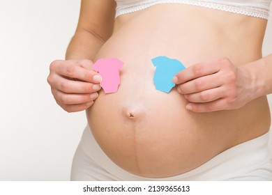 Shapes Of Pink And Blue Bodysuits On Young Adult Pregnant Woman Big Naked Belly. Guessing Future Baby Gender. Baby Expectation. Closeup. Isolated On Light Gray Background.