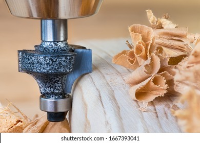 Shaping copying shank router bit clamped in chuck of a working machine tool. Sharp steel woodworking milling cutter with bearing forming a round edge on wood plank. Pile of twisted shavings. Joinery.