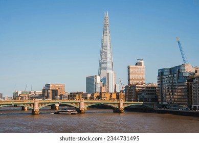 Shard tower amidst buildings with clear sky in background. Downtown district in city of London. Southwark bridge over river Thames on sunny day.
