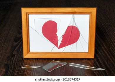 Shards Of Glass From A Photo Frame On A Dark Wooden Table. The Paper Heart Is Torn In Two.