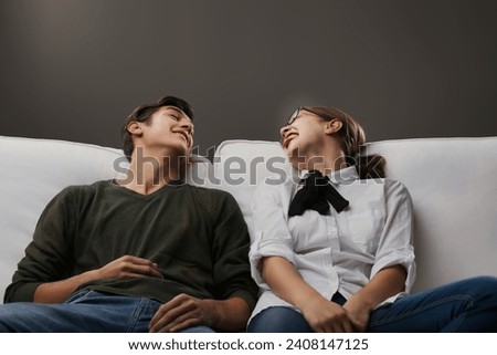 Shared laughter between a young man and woman lounging on a sofa captures a moment of genuine mirth