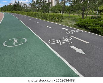 Shared running and cycling path in a city park on a sunny day. Distinct symbols on the pavement indicate a cyclist and a runner. The paths curve into the distance, surrounded by greenery and under a c