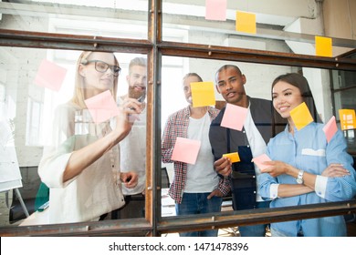 Sharing business ideas. Young modern people in smart casual wear using adhesive notes while standing behind the glass wall in the board room - Powered by Shutterstock