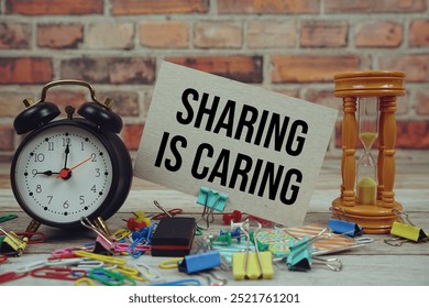 Sharing Is Caring text on paper card with alarm clock and stationary on wooden background