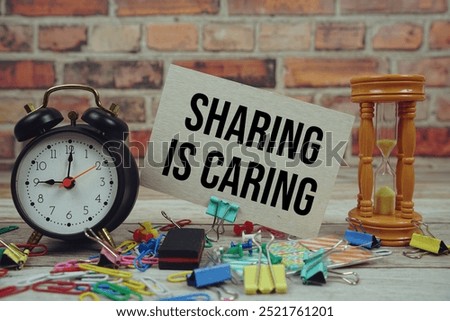 Sharing Is Caring text on paper card with alarm clock and stationary on wooden background