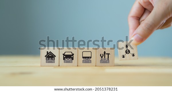 Sharing economy and smart consumption concept.\
People save money and share resources. Hand holds wooden cube with\
sharing symbol standing with car, house, equipment and computer\
sharing. Copy space.