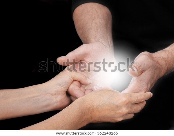 Sharing an Energy Experience -\
female healing mentor holding male students open hands with a\
bright light energy orb between on a black background and copy\
space