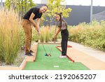 Sharing with golf experience. Cheerful young man teaching his daughter to play mini golf at the day time. Concept of friendly family