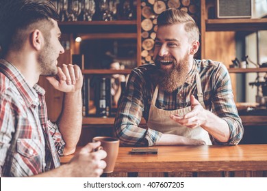 Sharing good news. Barista and his customer discussing something with smile while sitting at bar counter at cafe - Powered by Shutterstock