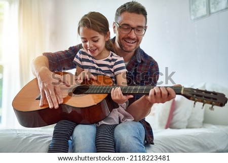Sharing his passion with his daughter. Shot of a little girl playing the guitar with her father.