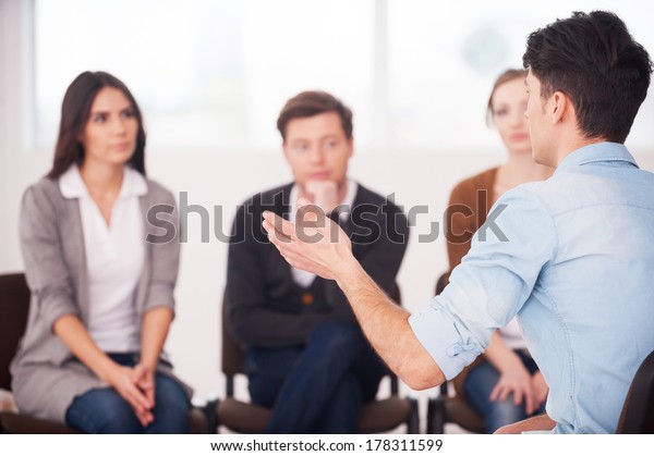 Sharing his problems with people. view of man\
telling something and gesturing while group of people sitting in\
front of him and\
listening