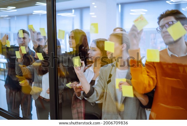 Sharing ideas concepts with papernote writing\
strategy on wall glass office. Business people meeting at office\
and use post it notes to share idea. Brainstorming concept.\
Planning, education,\
analysis