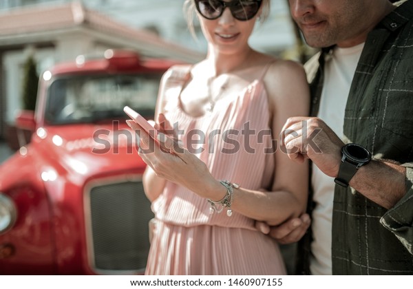 Sharing\
interests. Smiling woman showing her interested husband pictures on\
her smartphone standing with him in the\
street.