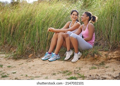 Sharing A Joke Between Friends. Two Friends Sitting Outside Laughing Together While Wearing Exercise Clothes.