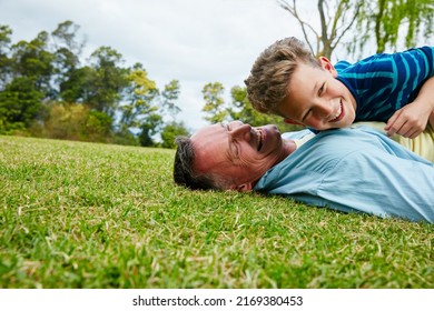 Sharing Moments Between Father And Son. Shot Of A Laughing Father And Son Lying On Grass.