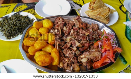 Sharing platter of a traditional Kenyan dish, Nyama Choma accompanied by kachumbari salad, sukuma wiki, chapati and roast potatoes. The roasted goat has been slow cooked outdoors. Eldoret, Africa.