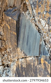 Sharp, angular fractures of a natural slate rock formation displaying smooth layered planes contrasting with rough, lichen-spotted edges.