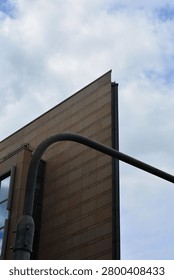 A sharp architectural corner of a tiled building against the sky, partially blocked by a curved metal pole