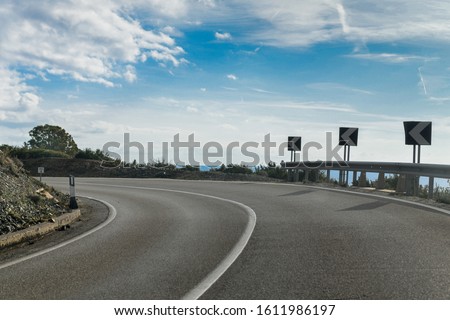 A sharp bend on an empty tarmac road with street signs. Edge of the cliff