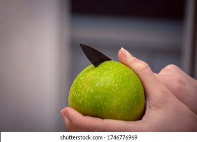 Sharp black knife cutting in a round green apple