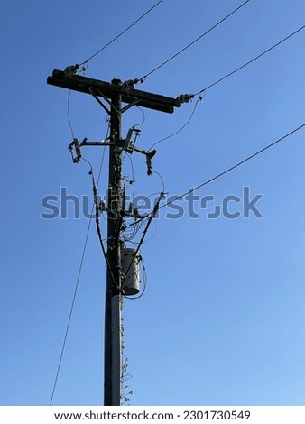 Sharp contrast between a silhouetted telephone pole with power lines and a transformer and the rich blue sky behind the pole. 