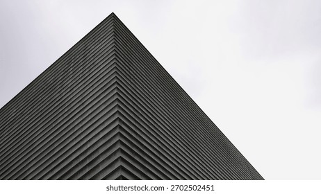 Sharp corner of a modern building with repeating horizontal metal fins against an overcast sky