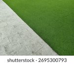 A sharp diagonal separation between vibrant green synthetic grass (turf) and light gray interlocking paver stones.