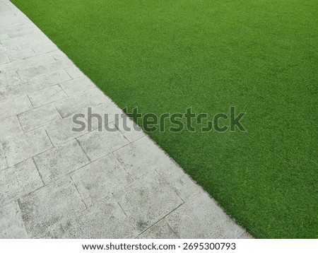 A sharp diagonal separation between vibrant green synthetic grass (turf) and light gray interlocking paver stones.