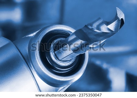 Sharp drill bit clamped in machine chuck with right angle head in blue tone on blurred tech background. Closeup a steel cutting instrument for drilling holes with hexagonal shank in power tool detail.