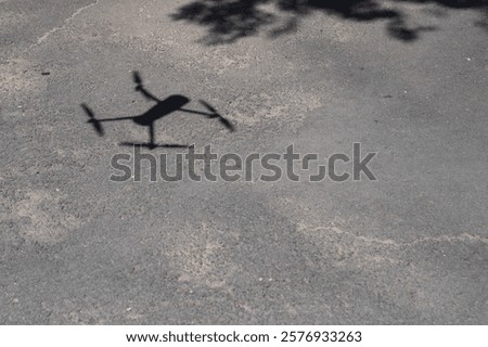 A sharp drone shadow contrasts against the rough texture of the asphalt.
A drone's shadow casts a haunting figure on a cracked asphalt .
