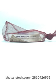 A sharp eye-level horizontal shot presents a side profile of a corporate souvenir mirror packed inside a small maroon mesh pouch over a bright white backdrop. The perspective shows the thickness of the translucent plastic object, with hints of the blue promotional text visible through the fine mesh layer of the bag. The loose top section of the net creates a dynamic shape, catching the soft studio light and adding depth to the minimalist composition. This versatile commercial asset is suitable for retail packaging guides, corporate branding case studies, or business gift design concepts. The bright overexposed lighting gives the photo a clean, clinical feel, allowing the dark red color of the pouch to stand out as the primary focus. Perfect for industrial marketing layouts, promotional item catalogs, or advertising agency blogs, this detailed shot effectively captures the simple structure of corporate merchandise.