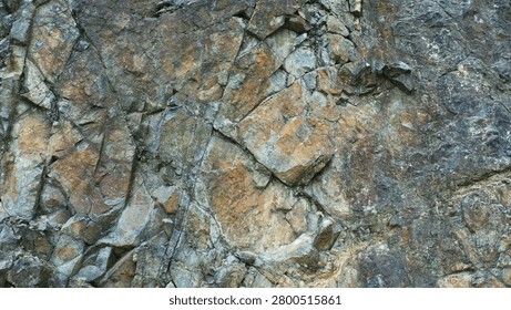 A sharp, high-resolution close-up of a rugged rock cliff face, showcasing intricate textures, mineral variations, and sharp edges in earthy tones.