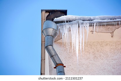 Sharp icicles hanging down from roof of the building. Icicles on facade of building, dangerous icicles melt on rooftop, risk of injury. Melting icicle danger for pedestrians
