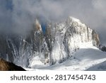 Sharp jagged alpine mountain needles wrapped in thick clouds and fresh snow cover