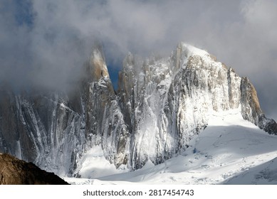 Sharp jagged alpine mountain needles wrapped in thick clouds and fresh snow cover