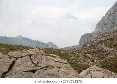 Sharp mountain peak emerges from the clouds above a rocky foothill with limestone boulders. Spring mountain landscape, Taurus mountains, Turkey.