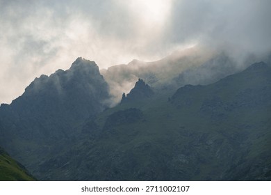 Sharp mountain peaks partially covered by mist and illuminated by dramatic natural light, creating a moody and atmospheric mountain scene