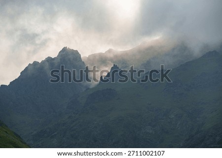 Sharp mountain peaks partially covered by mist and illuminated by dramatic natural light, creating a moody and atmospheric mountain scene