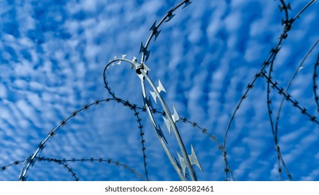 Sharp NATO-style barbed wire loops silhouetted against a blue sky with clouds, symbolizing security, control, and boundaries.