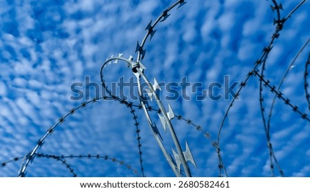 Sharp NATO-style barbed wire loops silhouetted against a blue sky with clouds, symbolizing security, control, and boundaries.