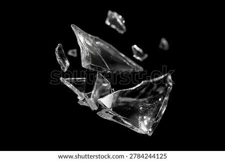 Sharp pieces of broken glass exploding and floating in mid-air against a dark black background. Highlights reflections on transparent shards.