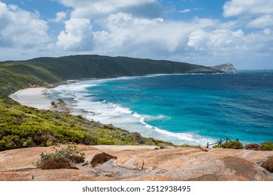 Sharp Point Lookout in Western Australia, featuring a rocky coastline, turquoise ocean waves, and a sandy beach. Dense green vegetation covers the hillsides under a cloudy sky. - Powered by Shutterstock