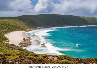 Sharp Point Lookout in Western Australia, featuring a rocky coastline, turquoise ocean waves, and a sandy beach. Dense green vegetation covers the hillsides under a cloudy sky. - Powered by Shutterstock