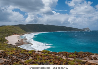 Sharp Point Lookout in Western Australia, featuring a rocky coastline, turquoise ocean waves, and a sandy beach. Dense green vegetation covers the hillsides under a cloudy sky. - Powered by Shutterstock