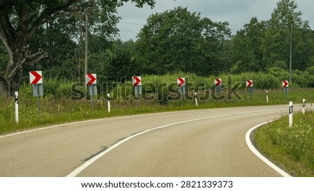 Sharp road curve marked by multiple red and white chevron signs in a rural landscape.