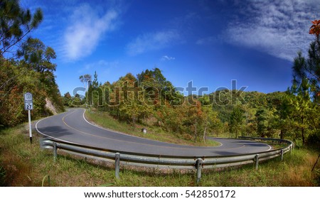 Sharp road curve for uphill to high mountains on blue sky background