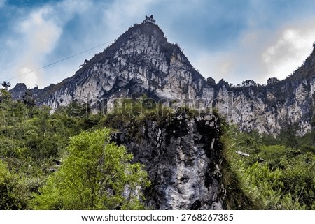 Sharp rocky mountain peak with a small structure built on the summit against a dramatic sky. Majestic limestone cliff landscape.
